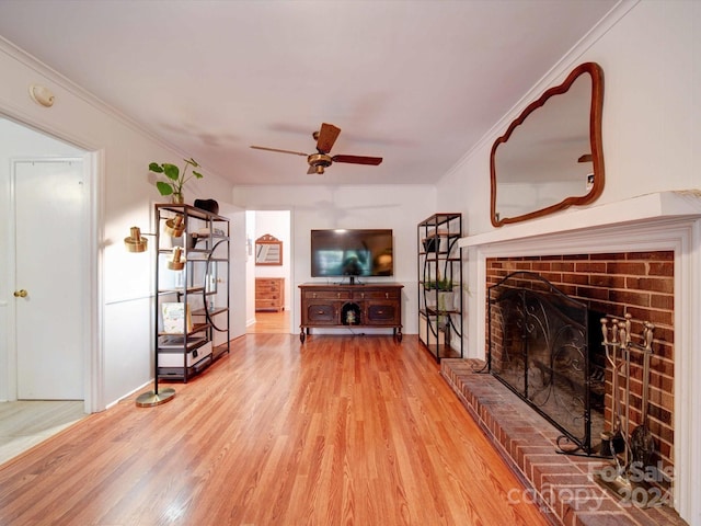 living room featuring ceiling fan, crown molding, a brick fireplace, and light hardwood / wood-style flooring