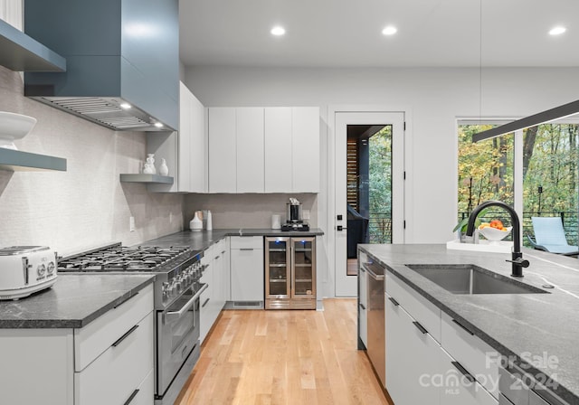 kitchen featuring wine cooler, white cabinets, appliances with stainless steel finishes, wall chimney exhaust hood, and sink