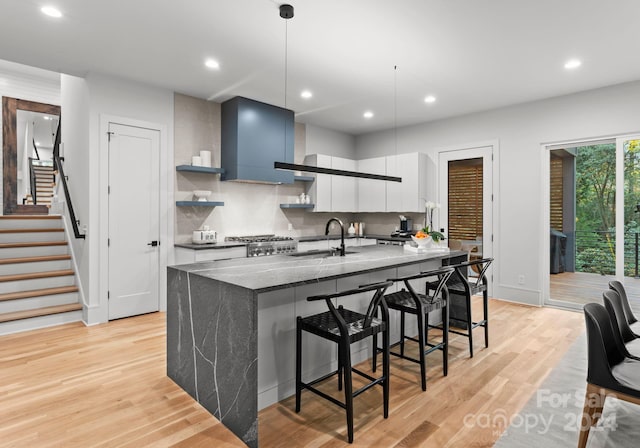 kitchen with hanging light fixtures, dark stone counters, sink, white cabinetry, and light hardwood / wood-style floors