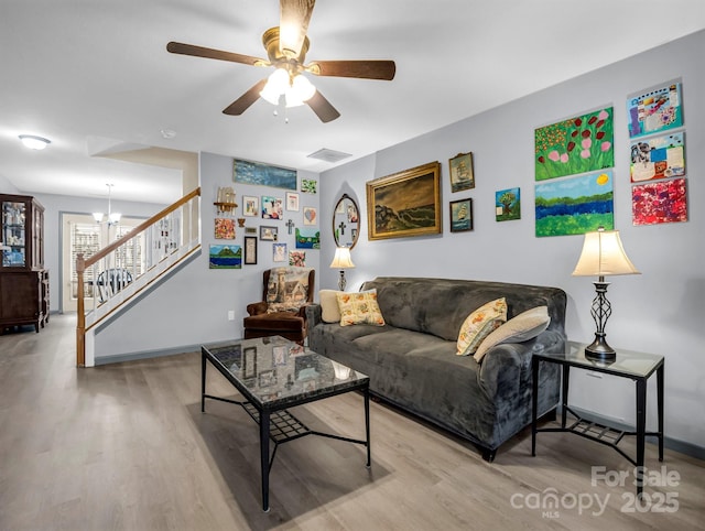 living room with light wood-type flooring and ceiling fan with notable chandelier