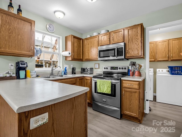 kitchen with sink, washing machine and dryer, kitchen peninsula, appliances with stainless steel finishes, and light wood-type flooring