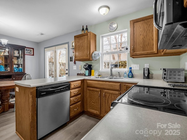 kitchen with stainless steel dishwasher, kitchen peninsula, sink, and light hardwood / wood-style flooring