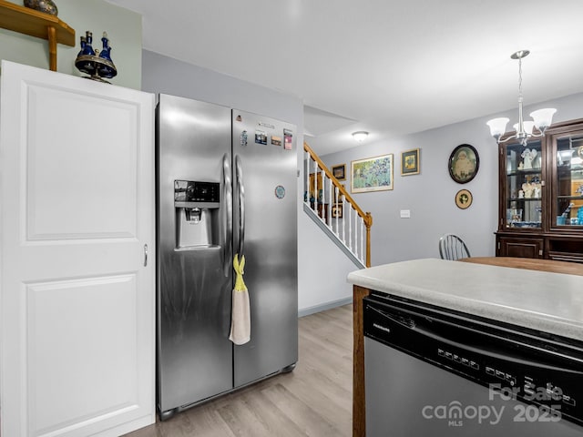 kitchen with appliances with stainless steel finishes, decorative light fixtures, an inviting chandelier, and light hardwood / wood-style floors