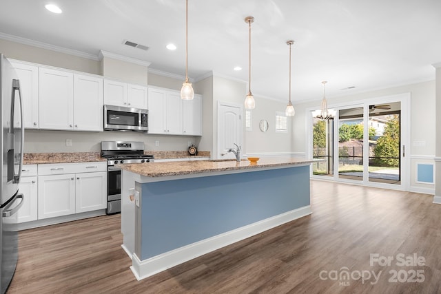 kitchen with light stone counters, visible vents, appliances with stainless steel finishes, ornamental molding, and wood finished floors