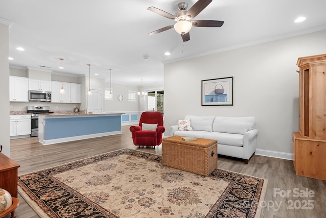 living area featuring recessed lighting, ceiling fan with notable chandelier, baseboards, light wood finished floors, and crown molding