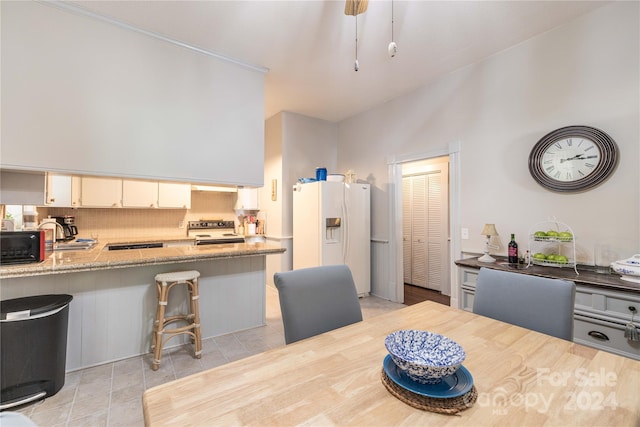 kitchen featuring stainless steel electric range, kitchen peninsula, decorative backsplash, white fridge with ice dispenser, and light stone countertops