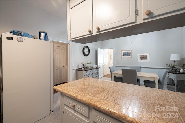 kitchen with white cabinetry, light tile patterned floors, and white fridge