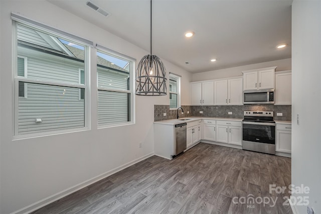 kitchen featuring stainless steel appliances, wood finished floors, a sink, visible vents, and decorative backsplash