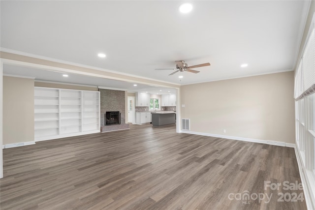 unfurnished living room featuring hardwood / wood-style floors, crown molding, a large fireplace, and ceiling fan