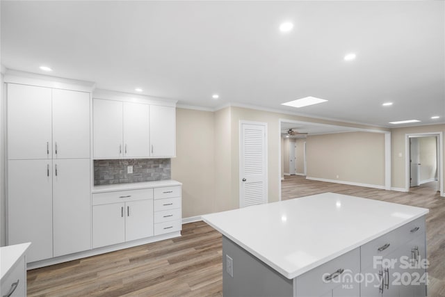 kitchen with backsplash, a center island, white cabinetry, light hardwood / wood-style floors, and ceiling fan