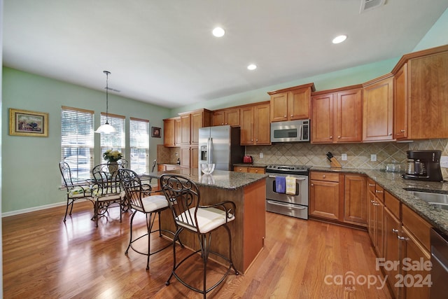 kitchen with a center island, stainless steel appliances, light hardwood / wood-style flooring, and hanging light fixtures