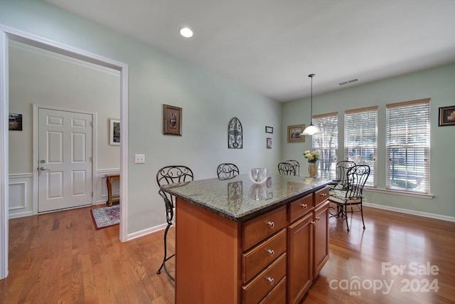 kitchen with a kitchen breakfast bar, dark stone counters, light hardwood / wood-style flooring, a center island, and hanging light fixtures