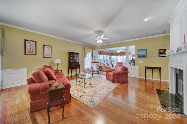 living room with ceiling fan, crown molding, a high end fireplace, and light wood-type flooring