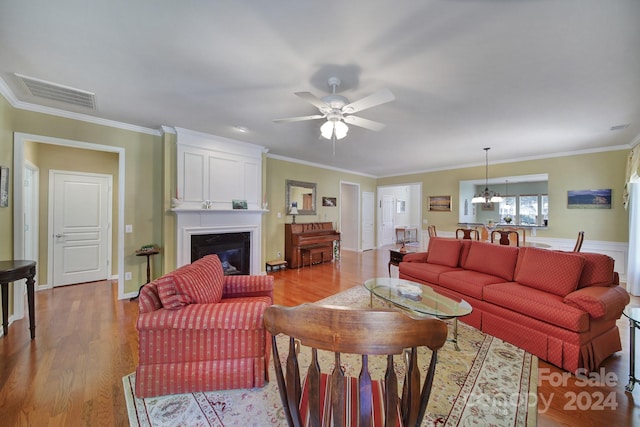 living room with ceiling fan with notable chandelier, ornamental molding, a fireplace, and light hardwood / wood-style flooring