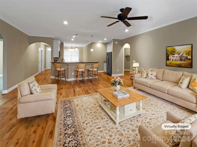 living room featuring ornamental molding, ceiling fan with notable chandelier, and light hardwood / wood-style floors