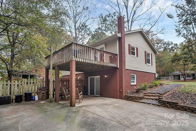 rear view of property with a deck, driveway, a carport, a chimney, and a patio area