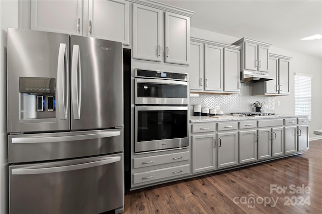 1568 Whitman Ct, York, SC 29745 - kitchen featuring appliances with stainless steel finishes, under cabinet range hood, gray cabinetry, dark wood-type flooring, and decorative backsplash