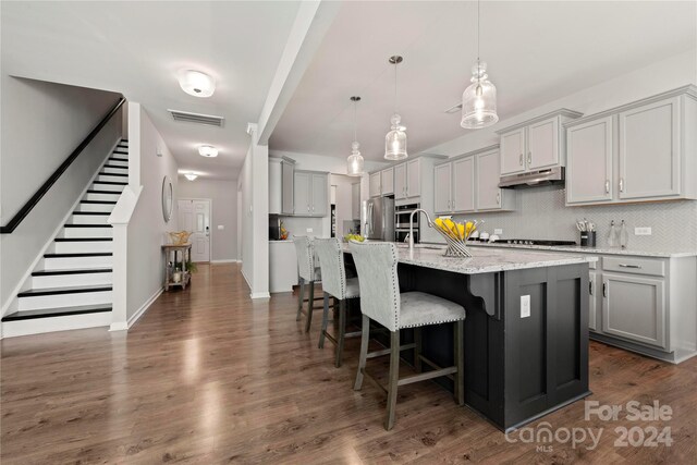 kitchen with a center island with sink, stainless steel fridge, decorative light fixtures, gray cabinets, and light stone counters