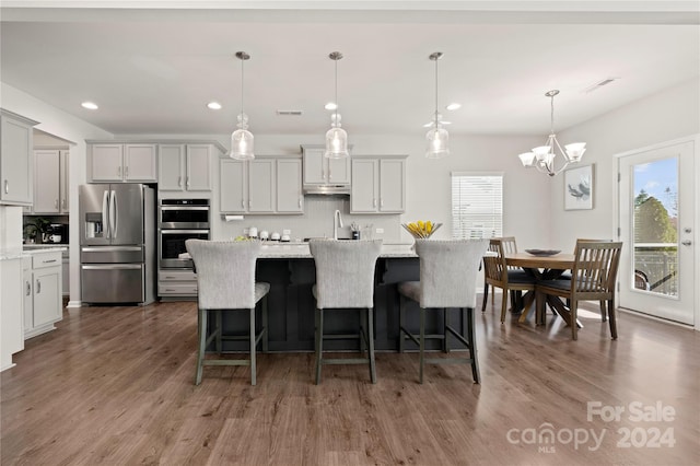 kitchen with stainless steel appliances, a wealth of natural light, pendant lighting, and a kitchen island with sink