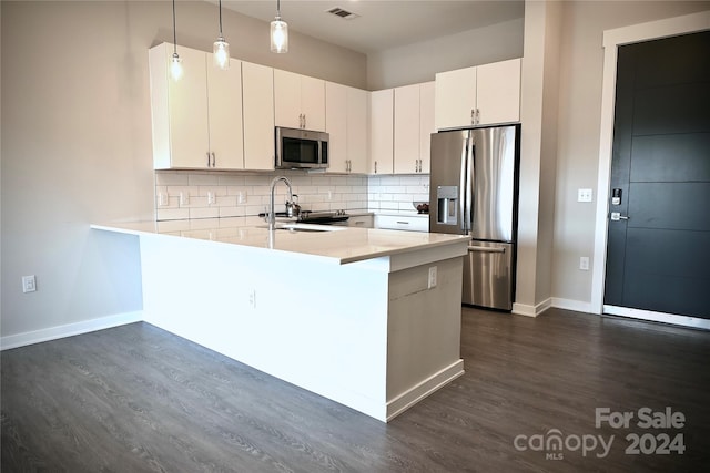 kitchen featuring appliances with stainless steel finishes, kitchen peninsula, white cabinetry, decorative light fixtures, and dark wood-type flooring