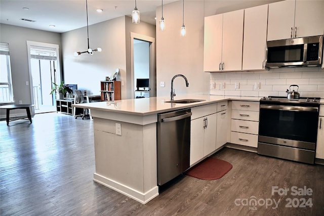 kitchen featuring kitchen peninsula, appliances with stainless steel finishes, dark wood-type flooring, sink, and decorative light fixtures