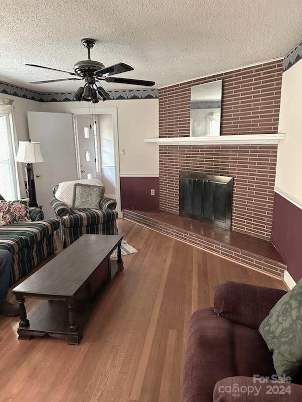 living room featuring hardwood / wood-style floors, ceiling fan, a textured ceiling, and a brick fireplace