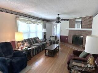 living room featuring a textured ceiling, hardwood / wood-style flooring, ceiling fan, and a brick fireplace