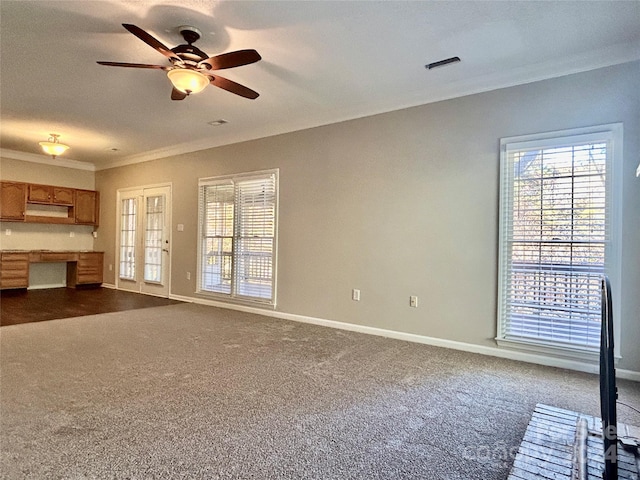 unfurnished living room with crown molding, built in desk, ceiling fan, and dark carpet