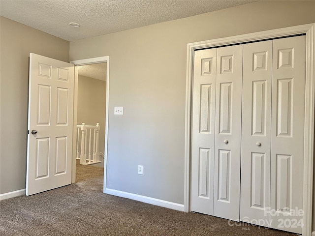 unfurnished bedroom with dark colored carpet, a textured ceiling, and a closet