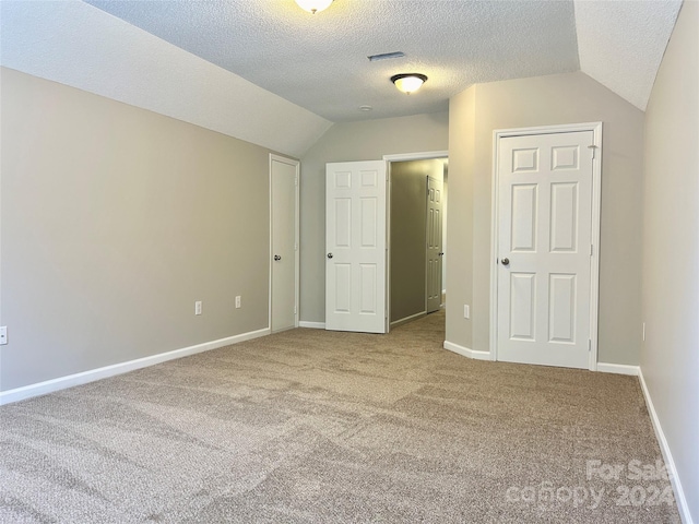 unfurnished bedroom with carpet flooring, a closet, a textured ceiling, and lofted ceiling