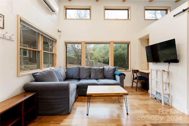 living room with a wall mounted air conditioner, light hardwood / wood-style flooring, and a healthy amount of sunlight