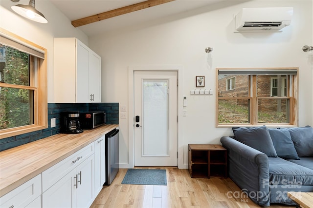 kitchen with wood counters, a wall mounted AC, lofted ceiling with beams, white cabinets, and light hardwood / wood-style floors