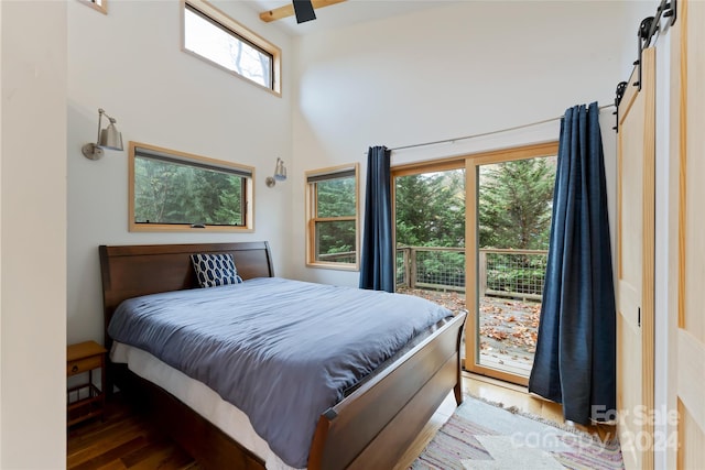 bedroom featuring hardwood / wood-style floors, a towering ceiling, ceiling fan, and a barn door