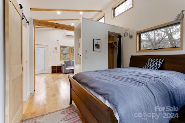 bedroom with beam ceiling, a barn door, light hardwood / wood-style flooring, and multiple windows