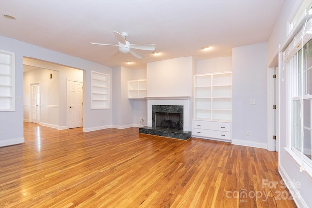 unfurnished living room with built in shelves, light hardwood / wood-style floors, a premium fireplace, and ceiling fan