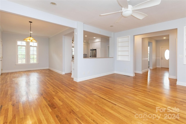 unfurnished living room with ceiling fan, built in features, light wood-type flooring, and crown molding