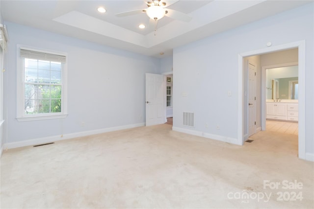 empty room featuring a tray ceiling, ceiling fan, and light colored carpet