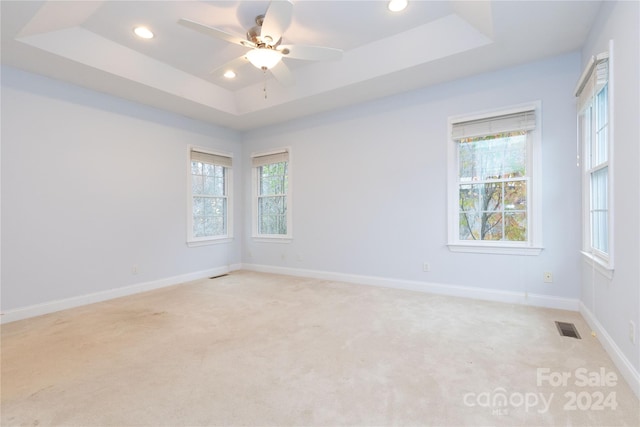 empty room with light carpet, a raised ceiling, and ceiling fan