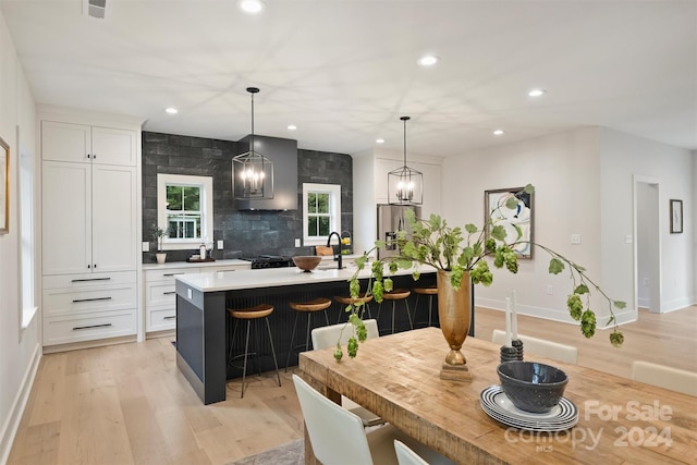 kitchen with a kitchen island with sink, decorative light fixtures, light wood-type flooring, and white cabinetry