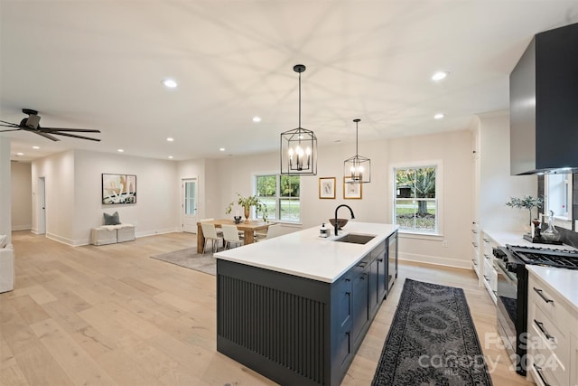 kitchen featuring sink, light wood-type flooring, white cabinetry, high end stainless steel range, and decorative light fixtures