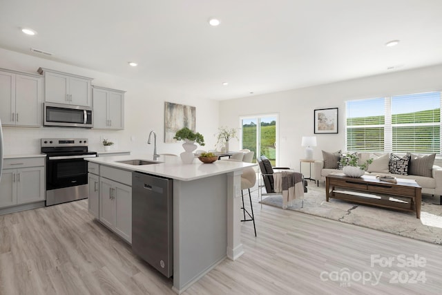 kitchen with a center island with sink, sink, appliances with stainless steel finishes, and gray cabinetry