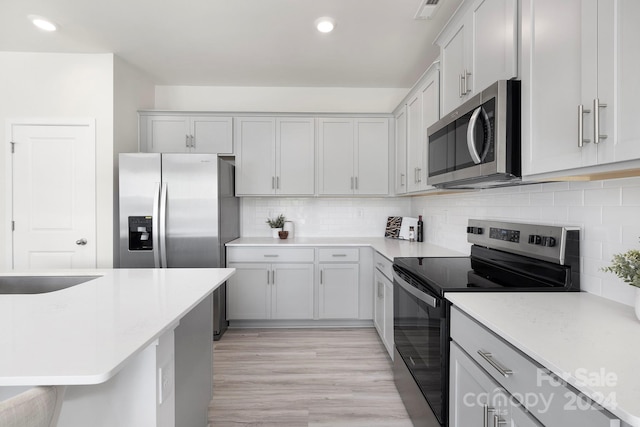 kitchen featuring stainless steel appliances, light wood-type flooring, and backsplash