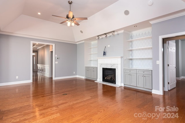 unfurnished living room with wood-type flooring, built in features, ceiling fan, crown molding, and a premium fireplace