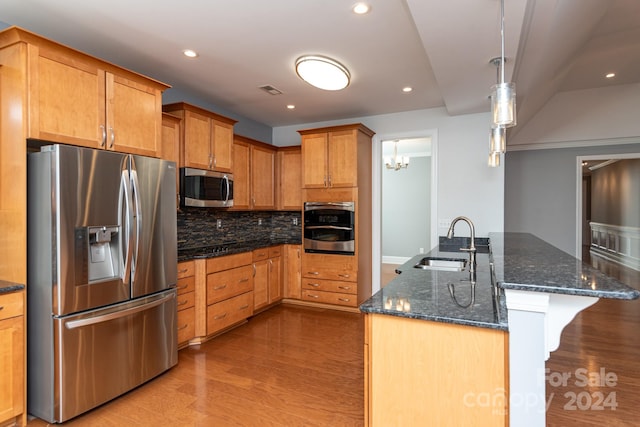 kitchen with hanging light fixtures, stainless steel appliances, dark stone counters, sink, and light hardwood / wood-style floors