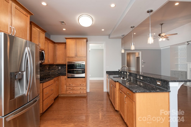 kitchen featuring hanging light fixtures, wood-type flooring, dark stone counters, stainless steel appliances, and sink