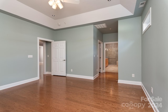 empty room featuring dark wood-type flooring, ceiling fan, and a tray ceiling