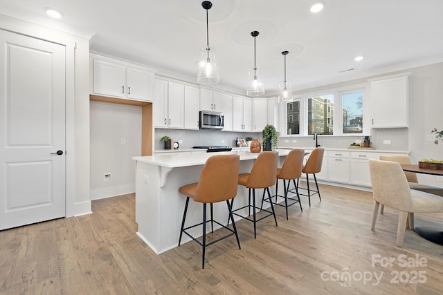 kitchen with pendant lighting, a breakfast bar, a center island, light hardwood / wood-style floors, and white cabinets