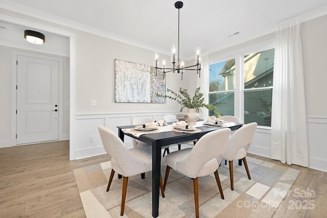 dining room with crown molding, an inviting chandelier, and light wood-type flooring