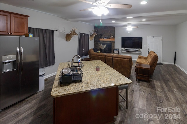 kitchen with a fireplace, dark hardwood / wood-style flooring, stainless steel refrigerator with ice dispenser, an island with sink, and ceiling fan