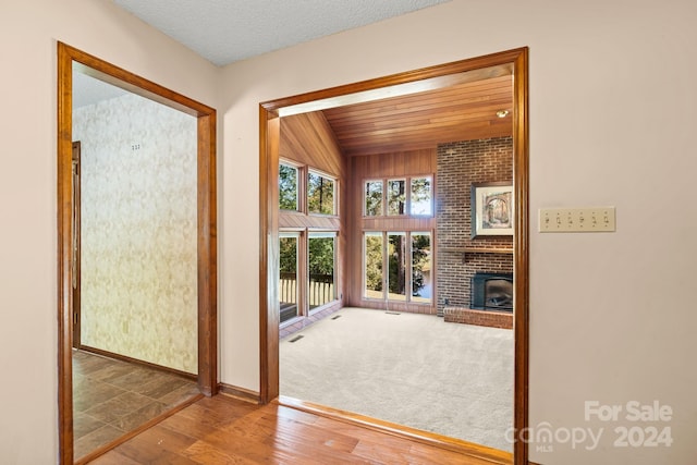 unfurnished living room featuring wood ceiling, a textured ceiling, hardwood / wood-style flooring, and a brick fireplace